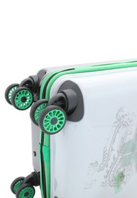 Valigia rigida con finitura bianca lucida, dettagli verdi e quattro ruote nere con un motivo circolare. Chiusura con zip e dettagli di design.