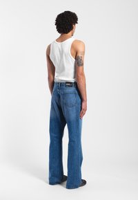 Flared blue denim jeans with a medium wash, featuring a standard five-pocket design and a black label on the waistband. Plain white tank top.