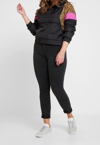 Černá zkrácená bunda s růžovými a leopardími akcenty, kombinovaná s černými skinny džíny a světle šedými teniskami. Obsahuje elastické manžety.