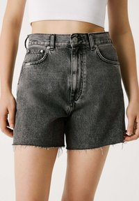 Shorts de mezclilla de tiro alto en gris oscuro con un acabado desgastado. Cuenta con un dobladillo deshilachado, cinco bolsillos y cierre de botón en la parte delantera.