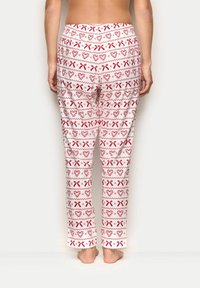 Pánské kalhoty na volný čas z bílé látky s červeným vánočním vzorem, který obsahuje srdce a mašle. Elastický pas, rovný střih, lehká textura.