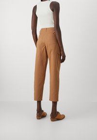 Hnědé bavlněné cargo kalhoty s rovnými nohavicemi, dvěma zadními kapsami a středním pasem, spárované s bílým žebrovaným tílkem a hnědými botami.