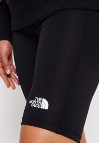 Černé sportovní šortky s těsným střihem, na lemu s bílým logem "The North Face". Hladká textura s elastickým pasem.