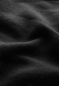Tessuto nero che mostra una superficie liscia e leggermente strutturata con pieghe e grinze sottili, enfatizzando il suo materiale e la sua trama.