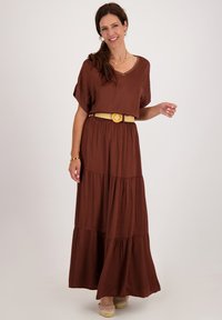 Bruine maxijurk met korte mouwen, V-hals, gelaagd ontwerp en een brede beige riem. Gladde textuur en vloeiende stof. Gekocht met lichte schoenen.