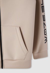 Felpa con zip beige dal tessuto morbido, tasca laterale e lettering nero lungo la manica. Presenta un orlo e polsini aderenti.