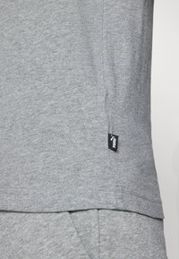 Grå bomulds T-shirt med en glat tekstur, prydet med et lille sort logo tag på den nedre søm og et enkelt rund hals design.