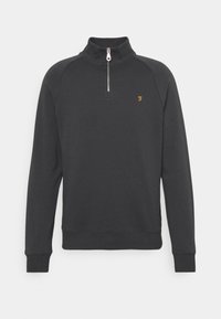 Sudadera negra de manga larga con medio zipper y pequeño logo dorado en el lado izquierdo del pecho, puños y dobladillo acanalados, cuello alto.