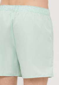 Pantaloni scurți de înot de culoare verde mentă deschisă, cu talie elastică, textură netedă și un design simplu, fără buzunare sau embellishments.