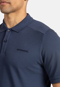 Námořnický polokošile s texturovanou látkou, s klasickým límcem, dvěma knoflíky a vyšitým logem "ROSSIGNOL" na levé hrudi.