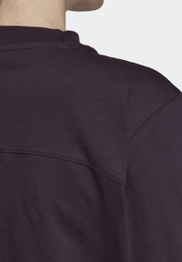 Primer plano de la parte superior de la espalda de una persona que lleva una camisa de color púrpura oscuro con detalles visibles en las costuras y un cuello redondo.