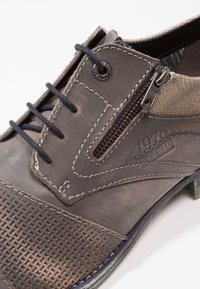 Chaussure gris foncé avec une tige en cuir texturé, des accents en tissu contrastants, une fermeture éclair et des détails de couture bleus.