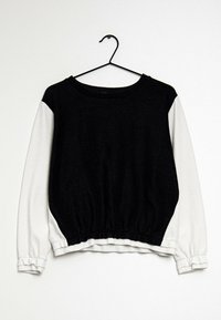 Pulóver de manga larga en blanco y negro con dobladillo fruncido, cuello redondo y tejido negro texturizado en el cuerpo, con mangas blancas lisas.