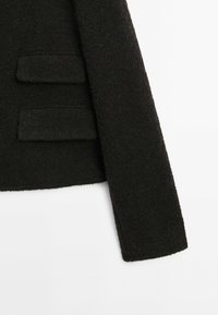 Black, textured jacket featuring two patch pockets on the front, with a clean silhouette and a slightly cropped sleeve design.