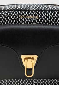 Μαύρη δομημένη τσάντα χειρός με υφασμάτινο λευκό και μαύρο μοτίβο στην αναδιπλούμενη θήκη. Κλείσιμο με χρυσό εξάρτημα που τονίζει το κλείσιμο. Το όνομα της επωνυμίας είναι ανάγλυφο.