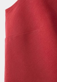 Tissu rouge avec un détail de couture diagonale, montrant la texture et les coutures sur une surface lisse et de couleur unie.