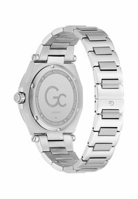 Suds sudraba nerūsējošā tērauda pulkstenis ar astoņstūra korpusu, integrētu aproci un plakanu safīra kristālu. Aizmugurē redzams zīmola logo un informācija.