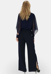 Granatowy dwuczęściowy zestaw składający się z półprzezroczystej bluzki z rękawami-kapami oraz spodni szerokich nogawkach, obie rzeczy mają rozcięcia po bokach i gładkie wykończenie.