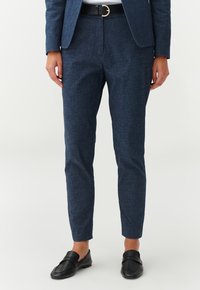 Pantalones ajustados de color azul oscuro hechos de un tejido texturizado, que presentan un corte slim, bolsillos laterales y un cinturón negro con una hebilla dorada.