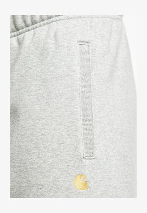 Pantalones de chándal de color gris claro, confeccionados con una tela suave, que cuentan con un bolsillo vertical y un pequeño logotipo bordado en dorado. Cintura elástica para un mejor ajuste.