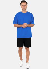 T-shirt en coton bleu associé à un short noir. Le T-shirt a des manches courtes et un col rond. Des baskets blanches complètent la tenue.