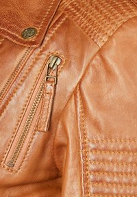 Brown leather jacket featuring a zippered pocket and textured stitching along the shoulders. Metallic hardware complements the design.