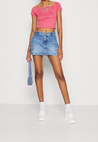 Růžový crop top, modrá džínsová mini sukně s předními kapsami, bílé platformové boty na podpatku a šedá vzorovaná kabelka.