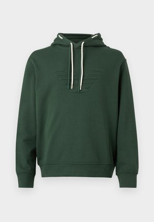 Tamsiai žalias gobtuvu megztinis su baltais raišteliais ir reljefiniu sparnuotu logotipu ant krūtinės, ilgos rankovės, su riboto audinio rankogaliais ir apačia.