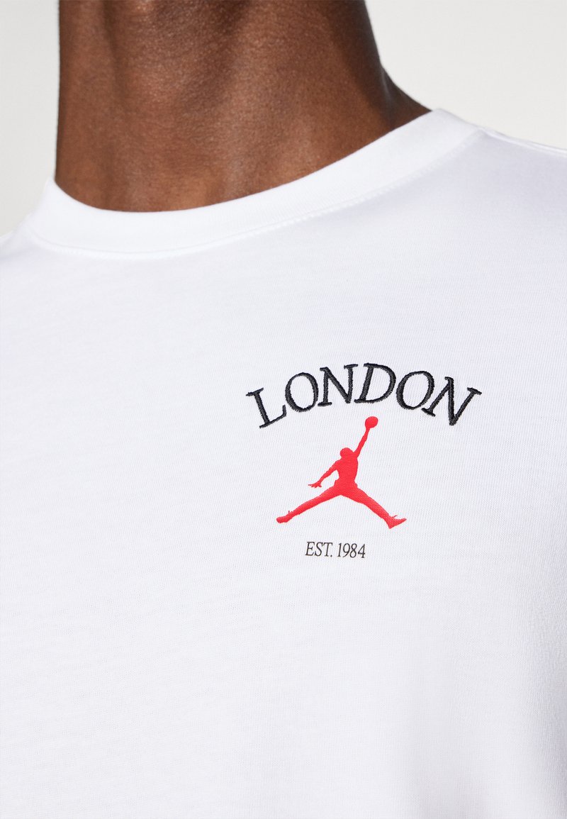 T-shirt en coton blanc avec le texte "LONDON" en noir et un logo Jumpman rouge, avec "EST. 1984" en petite police noire en dessous.