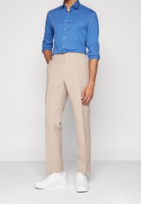 Camicia button-up azzurro chiaro con maniche lunghe, abbinata a pantaloni di lino beige. Completata con sneaker bianche, creando un outfit casual e moderno.