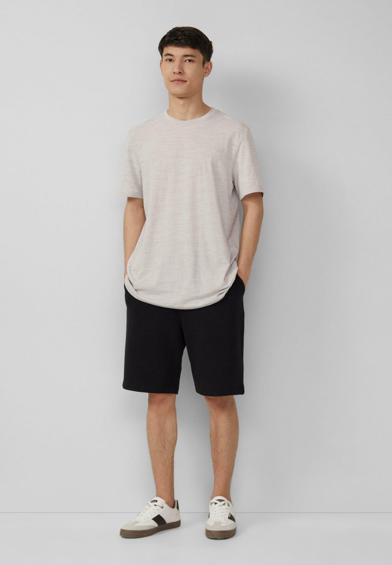 T-shirt à manches courtes gris clair avec une coupe décontractée, assorti à un short noir. Porté avec des baskets blanches et grises avec des accents noirs.