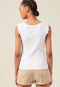 Vit ribbad ärmtröja med scalloped ögonlappdetaljer på ärmarna. Matchat med ljusbeige shorts med rullad fåll.