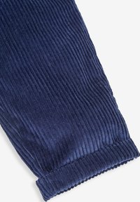 Marineblauwe corduroy stof met verticale ribbels. Heeft een ribboord aan de onderkant, wat zorgt voor een gestructureerde en textuurrijke uitstraling.