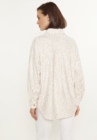 Witte blouse met lange mouwen en een subtiele luipaardprint in beige tinten, voorzien van een kraag, knopenmanchetten en een gebogen zoom.