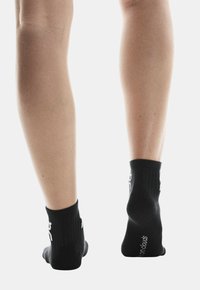 Calze sportive nere con un bordo a costine e un dettaglio del logo bianco, aderiscono bene ai piedi con una texture liscia e senza motivi visibili.
