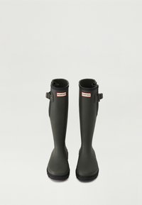 Botas de lluvia de goma verdes con una textura suave, de altura hasta la mitad de la pantorrilla y con hebillas laterales ajustables. Presenta una etiqueta de la marca en la parte frontal.