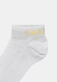 Άσπρη κάλτσα μέχρι τον αστράγαλο φτιαγμένη από μείγμα βαμβακιού, με κίτρινο λογότυπο "SKECH" ραμμένο στο περιθώριο. Λείος υφή με ριμπ κορυφή.
