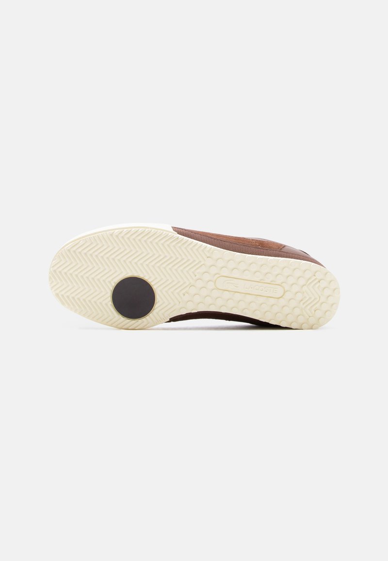 Zool van een bruine sneaker met gestructureerd beige rubber, een ronde zwarte grip bij de teen en het geperste Lacoste-logo op het booggebied.