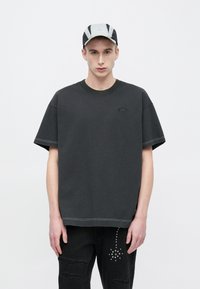 Túltengő fekete pamut póló bordázott nyakkivágással és finom logóval; párosítva hasított fekete farmerrel, amely ezüst szegecsekkel díszített.