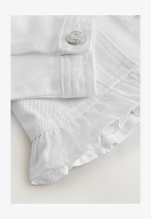 Közelkép egy fehér szöveten, ezüst gombbal és fodros szegéllyel egy textúrált ruházaton.