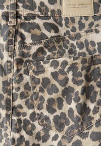 Tejido de mezclilla con estampado de leopardo que presenta un bolsillo y costuras en contraste. La paleta de colores incluye tonos marrones, negros y manchas en un fondo claro.