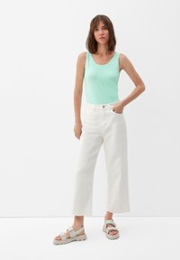 Mintgrünes ärmelloses Oberteil, weiße weitgeschnittene Jeans und hellgraue Sandalen mit dicker Sohle und verstellbaren Riemen. Einfaches, lässiges Outfit.