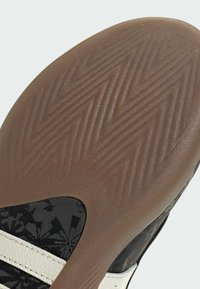 Λαστιχένια σόλα παπουτσιού με υφή καφέ επιφάνειας· μαύρα υφασμάτινα πάνελ με λουλουδάτο σχέδιο· λευκές ρίγες και λείες λευκές λεπτομέρειες.