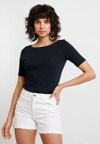 Svart tettsittende t-skjorte med rund halslinning, korte ermer og myk tekstur, kombinert med hvite denimshorts med oppbrettede bukseben.
