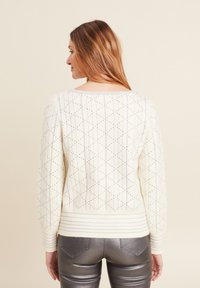 Maglione color crema con un motivo a diamante testurizzato, polsini e orlo a coste, e una scollatura ampia. Indossato con pantaloni argentati lucidi.