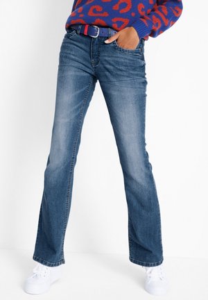 Jeans acampanados de mezclilla azul con una cintura de subida media, ligero desvanecimiento y cinco bolsillos, combinados con zapatillas blancas y un suéter estampado.