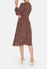 Blommig midi-klänning med långa ärmar, mörk bakgrund, rosa och gröna mönster, midjedetalj, tillsammans med vita klacksandaler med blockklack.