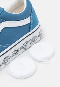 Modré plátěné tenisky s bílými akcenty, gumovou podrážkou a vzorem žáby na straně. Dodáváno se dvěma bílými kulatými tkaničkami.