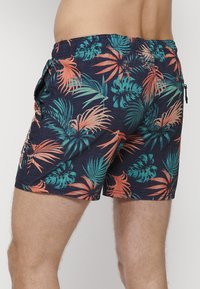 Pantaloni scurți de înot pentru bărbați cu un fundal bleumarin și modele de frunze tropicale în nuanțe de verde și corai. Dispun de o talie elastică și buzunare laterale.