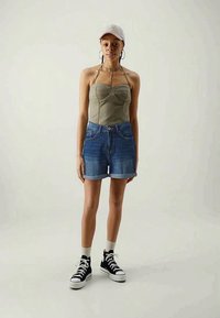 Top grigio senza maniche con un design strutturato, abbinato a pantaloni corti in denim blu e sneakers nere alte. Un cappellino chiaro completa l'outfit.